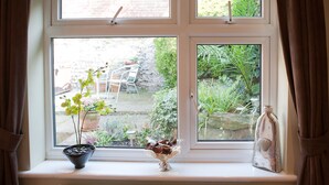 A window with a view of a garden, a potted plant, and a decorative item on the windowsill. - Sea Spray (Brighton)