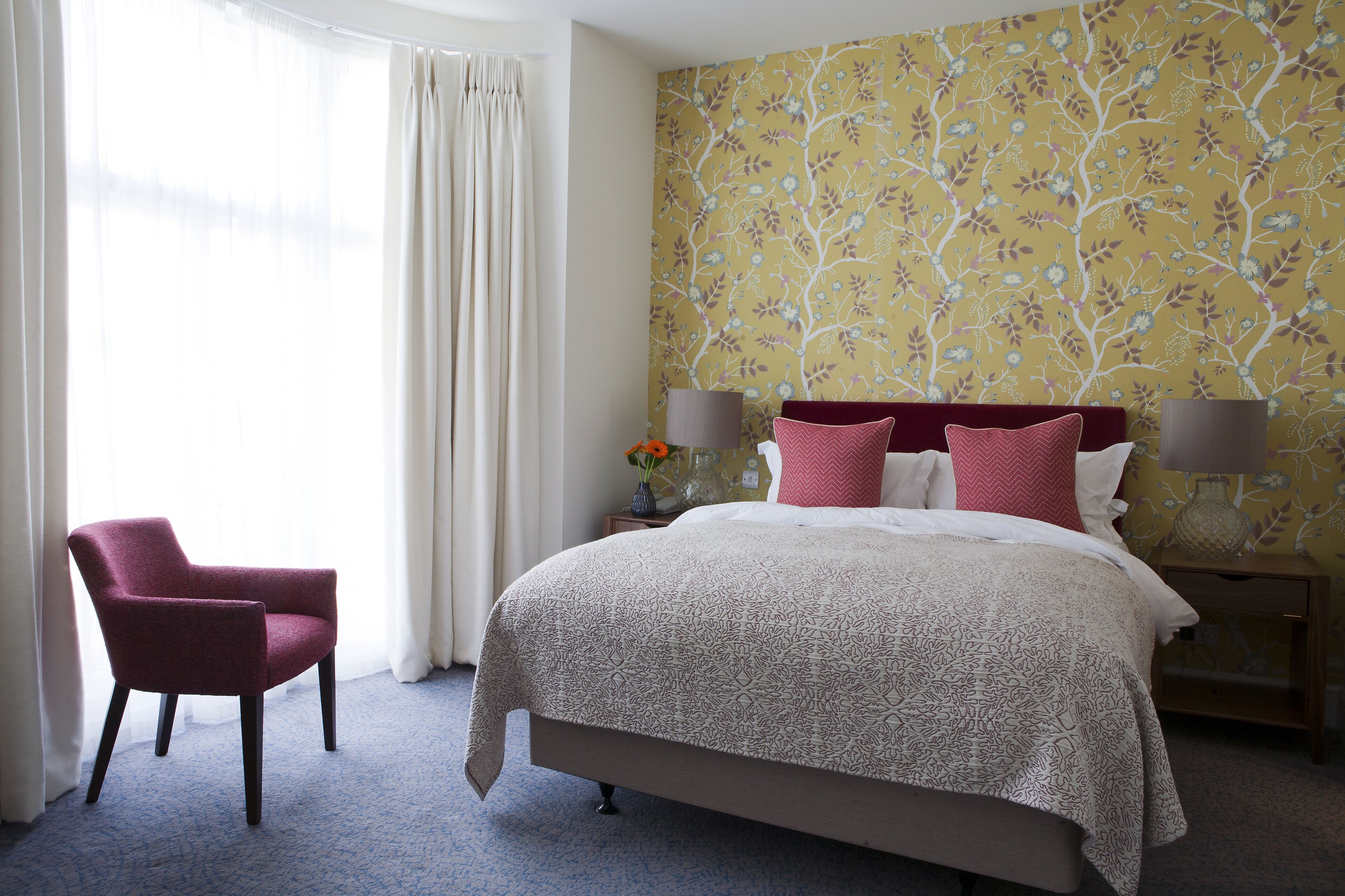 A hotel room with a bed, a chair, a nightstand, and a window with curtains.