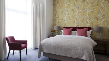 A hotel room with a bed, a chair, a nightstand, and a window with curtains.