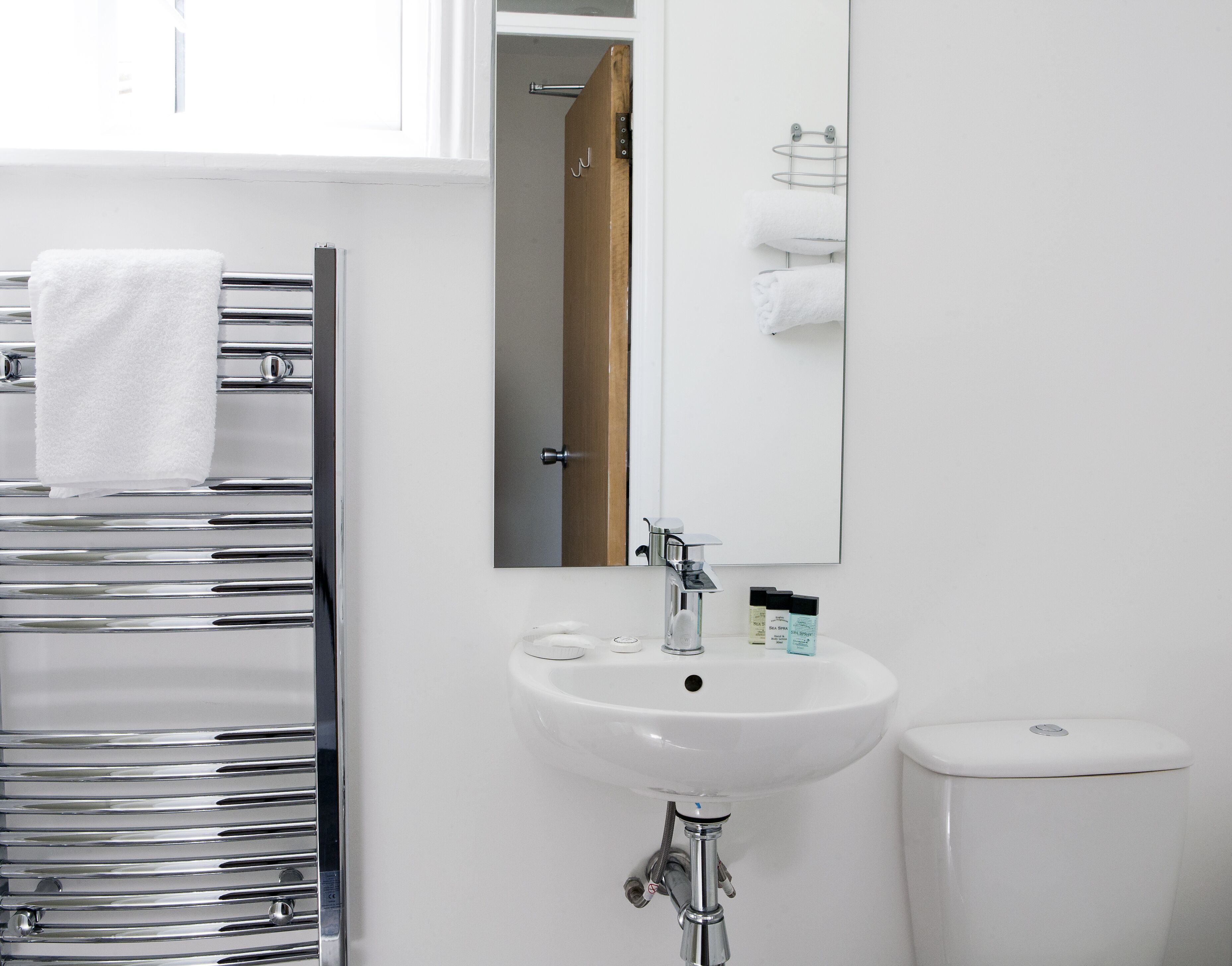A modern bathroom with a chrome towel rack, a white sink, and a toilet.