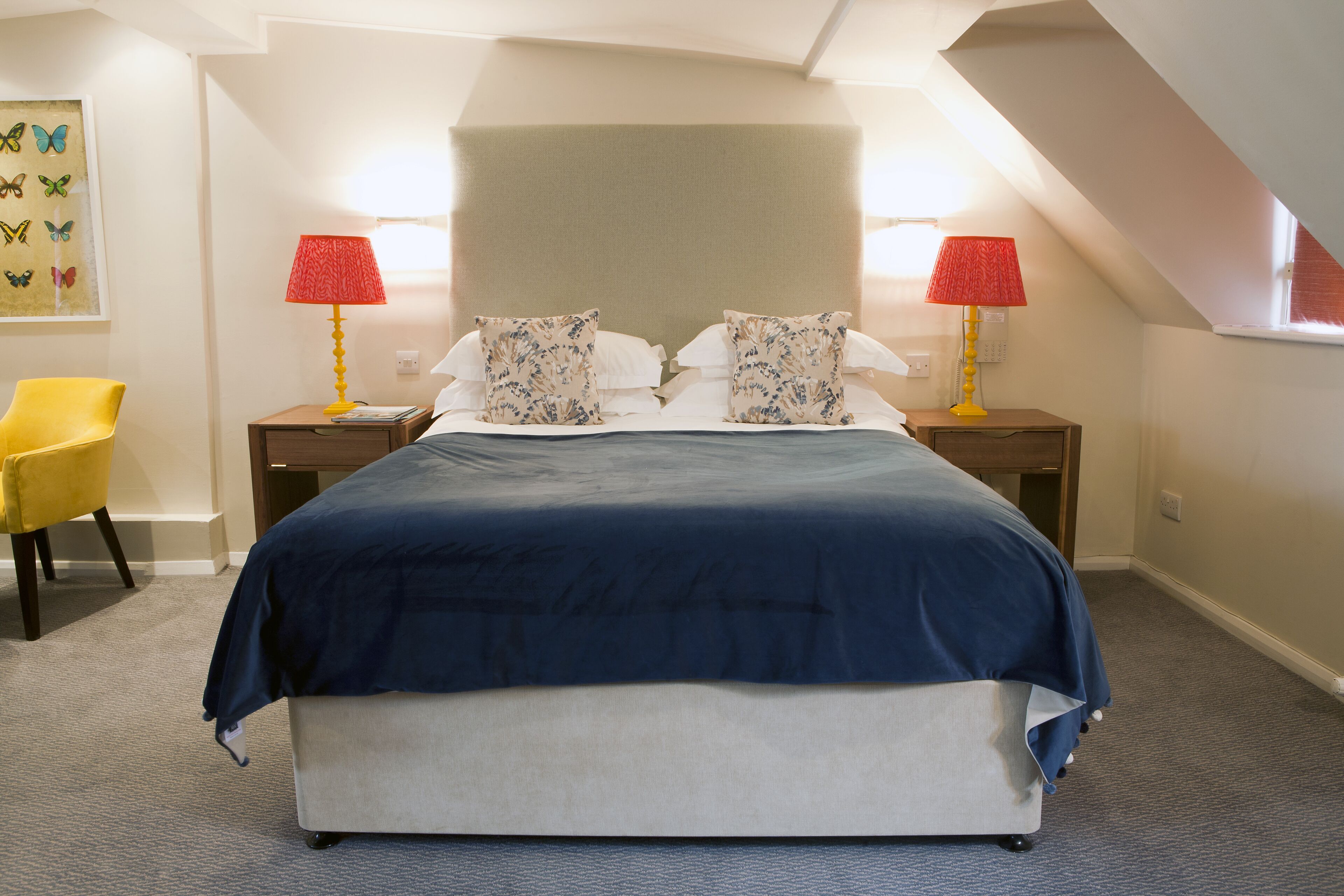 A bedroom with a large bed, two nightstands with lamps, a chair, and a wall art piece.