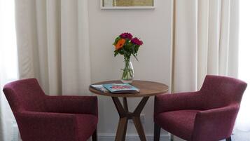 Una habitación con dos sillones rojos, una mesita redonda con un florero y una obra de arte con una mariposa enmarcada en la pared.