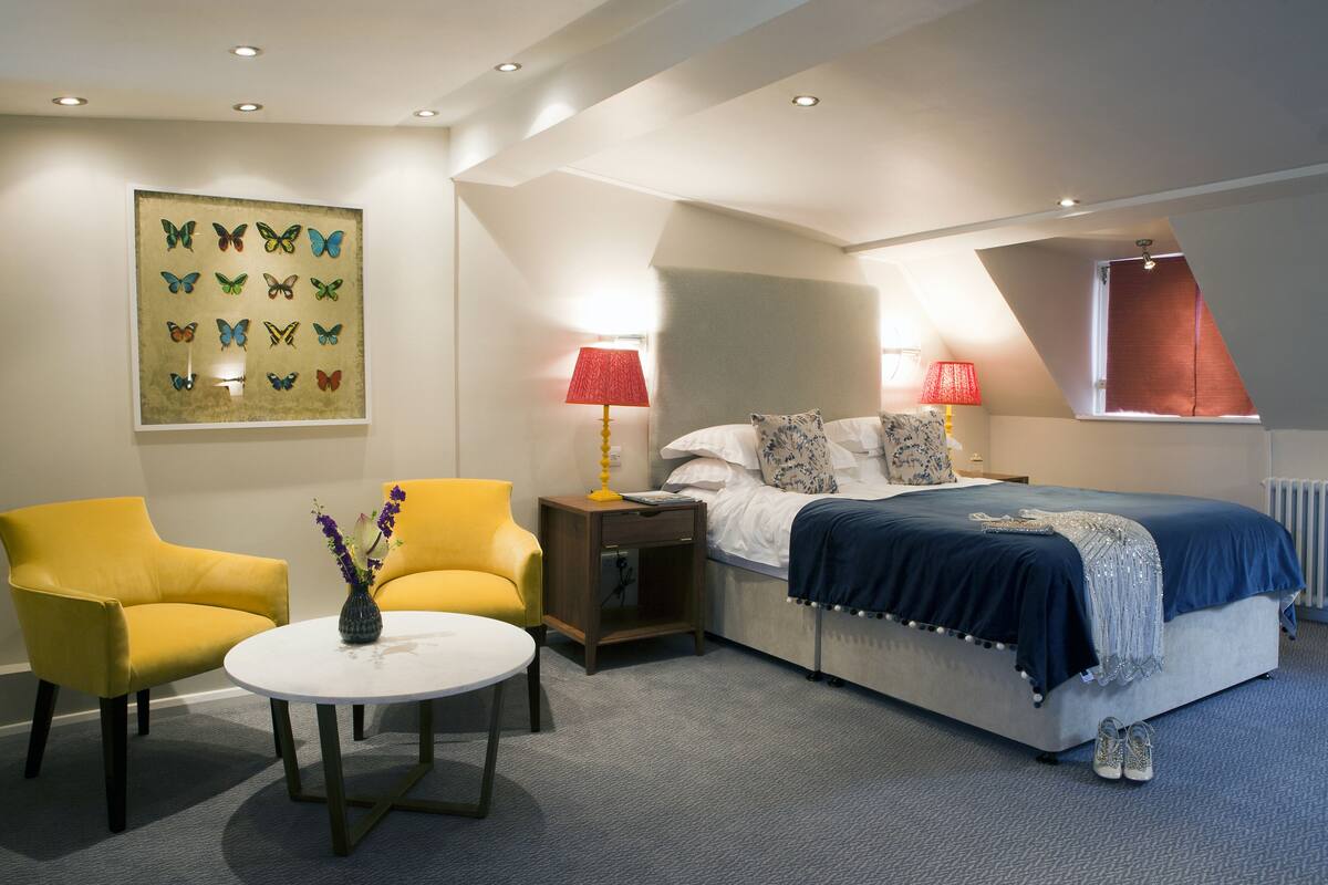 A bedroom with a bed, two chairs, a nightstand, a lamp, and a painting on the wall.
