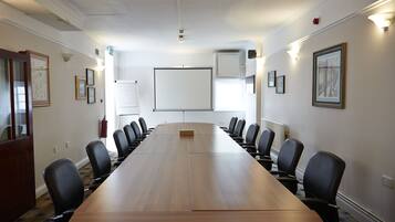 A conference room with a long table, black chairs, a whiteboard, framed pictures, and a fire extinguisher.