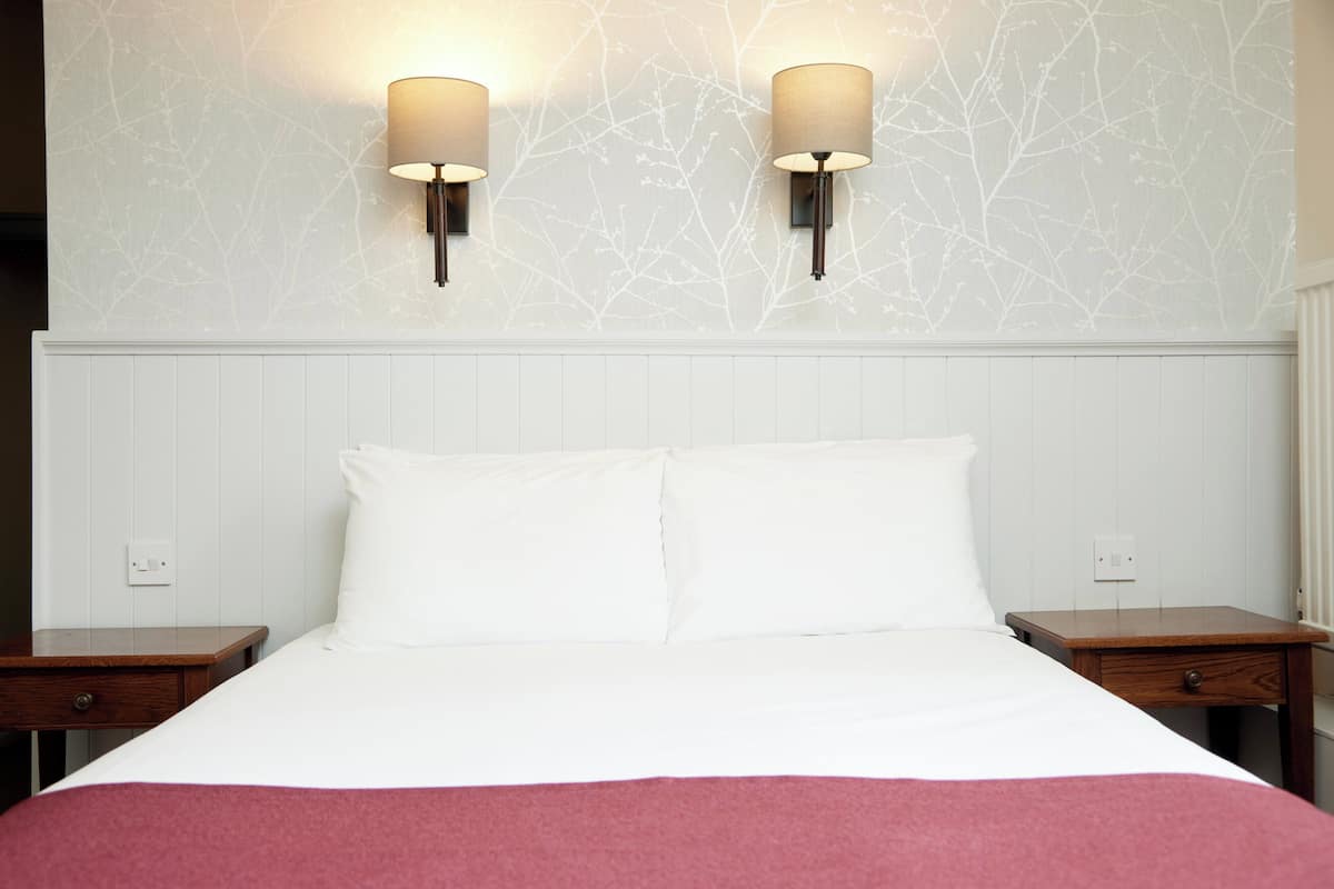 A hotel room with a large bed, two nightstands, and wall-mounted lamps.