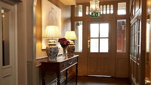 Un pasillo con suelo de madera, una mesa con lámparas y jarrones, y una puerta con letrero de salida verde.