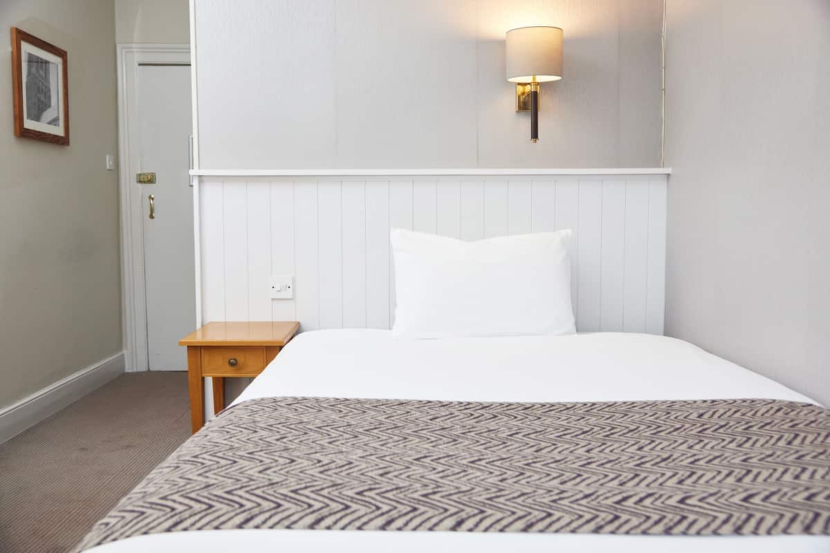 A hotel room with a bed, a nightstand, a wall-mounted lamp, and a door.