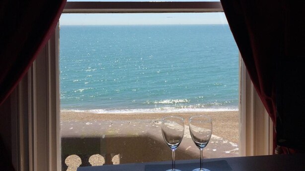 Una mesa con dos copas de vino vacías y vista al océano a través de una ventana con cortinas rojas.
