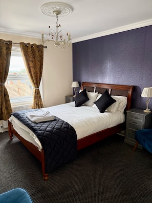 A neatly made bed with a dark quilt, a wooden headboard, and multiple pillows. - Atlanta Guesthouse (Eastbourne)