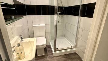 A bathroom with a glass-enclosed shower, a toilet, and a sink with a soap dispenser.