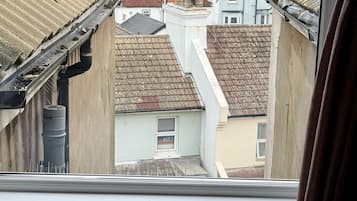 A view through a window of a residential area with multiple buildings, a visible gutter, and a radiator.