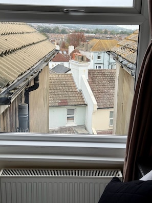 A view through a window of a residential area with multiple buildings, a visible gutter, and a radiator. - Atlanta Guesthouse (Eastbourne)