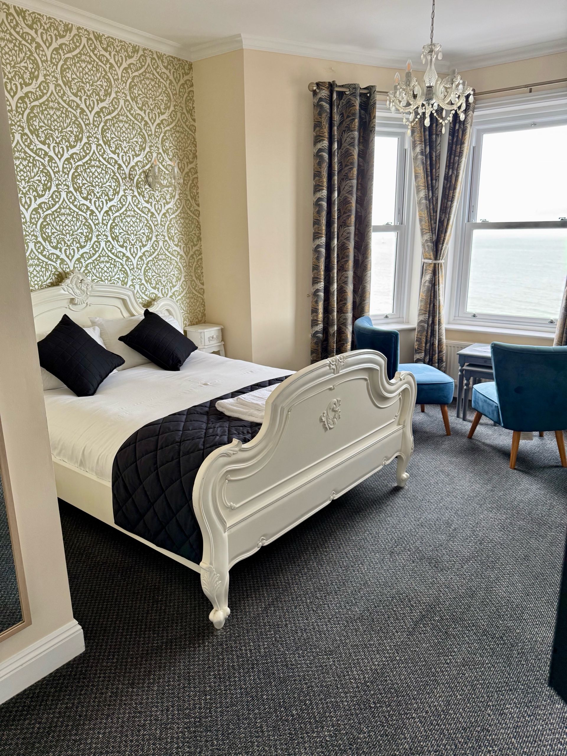 A hotel room with a large bed, a desk, and a view of the sea.