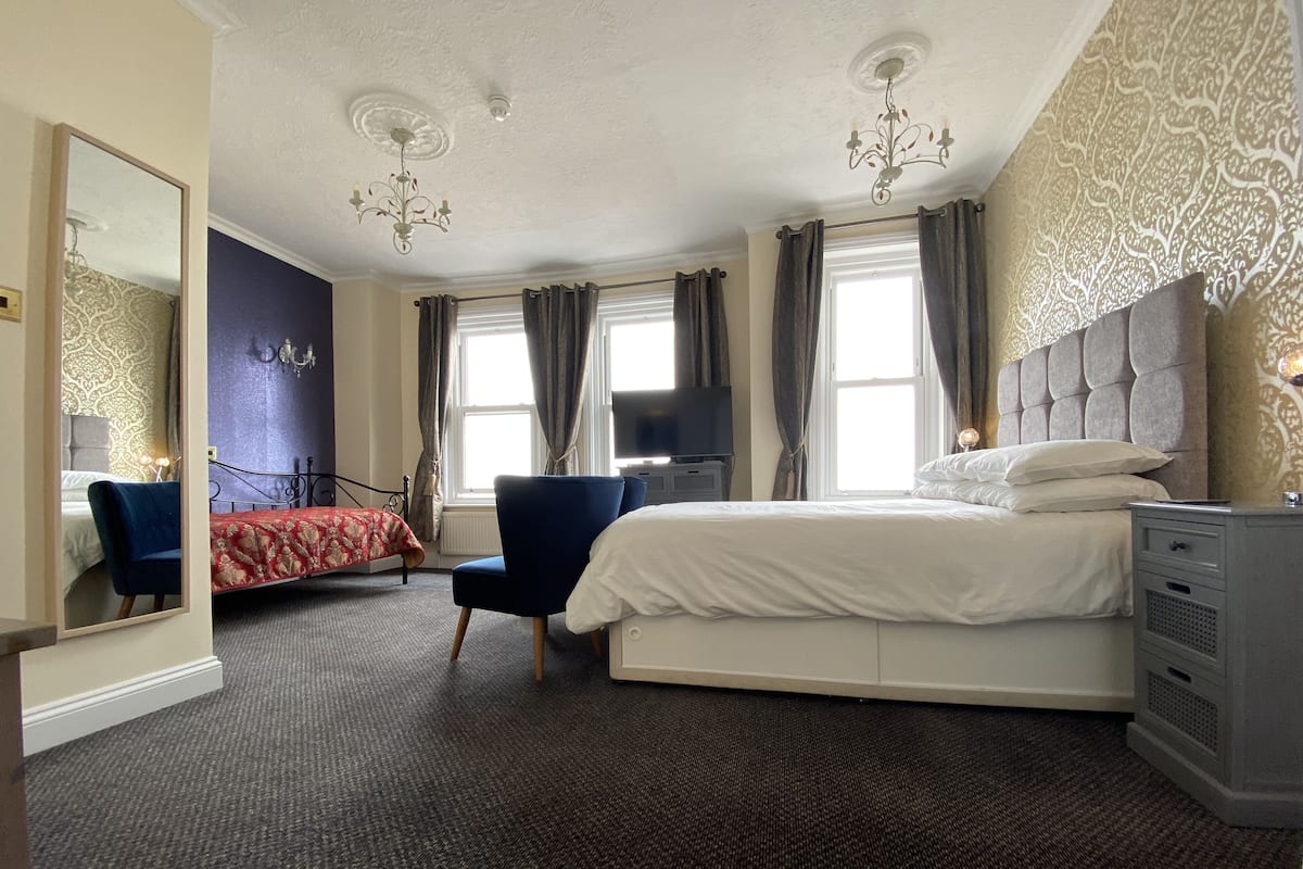 A hotel room with a large bed, a chair, a desk, a TV, and a mirror.