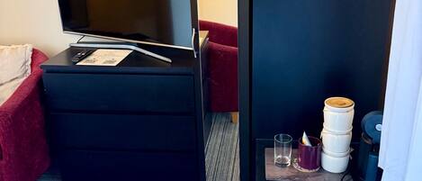 A hotel room with a bed, a television, a desk with a remote control, a mirror, and a small table with a glass and a cup.