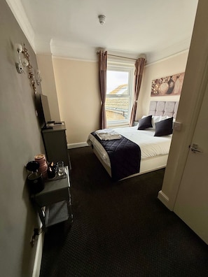 A hotel room with a bed, a desk, a window with curtains, and a painting on the wall. - Atlanta Guesthouse (Eastbourne)