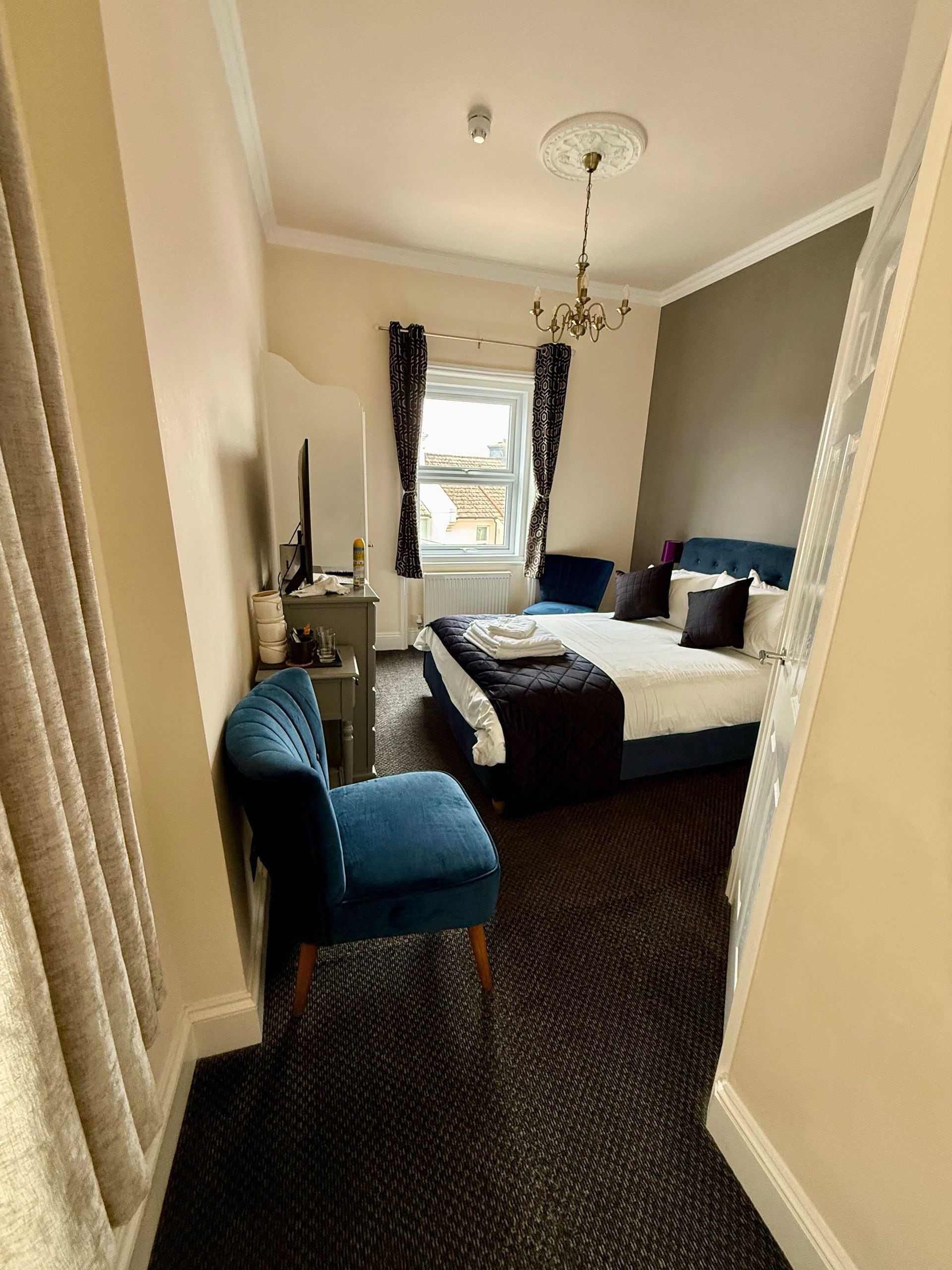 Een hotelkamer met een bed, een bureau, een stoel, een raam met gordijnen en een kroonluchter.