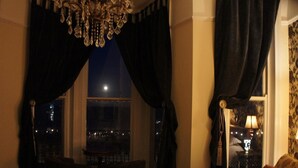 Habitación de hotel con una cama grande, una araña y vistas de la ciudad de noche.