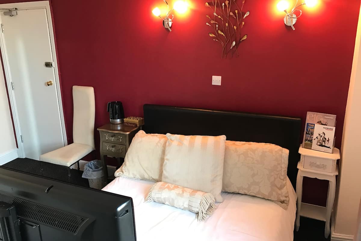 A hotel room with a bed, a nightstand with a coffee maker, a wall-mounted light fixture, and a magazine on the nightstand.