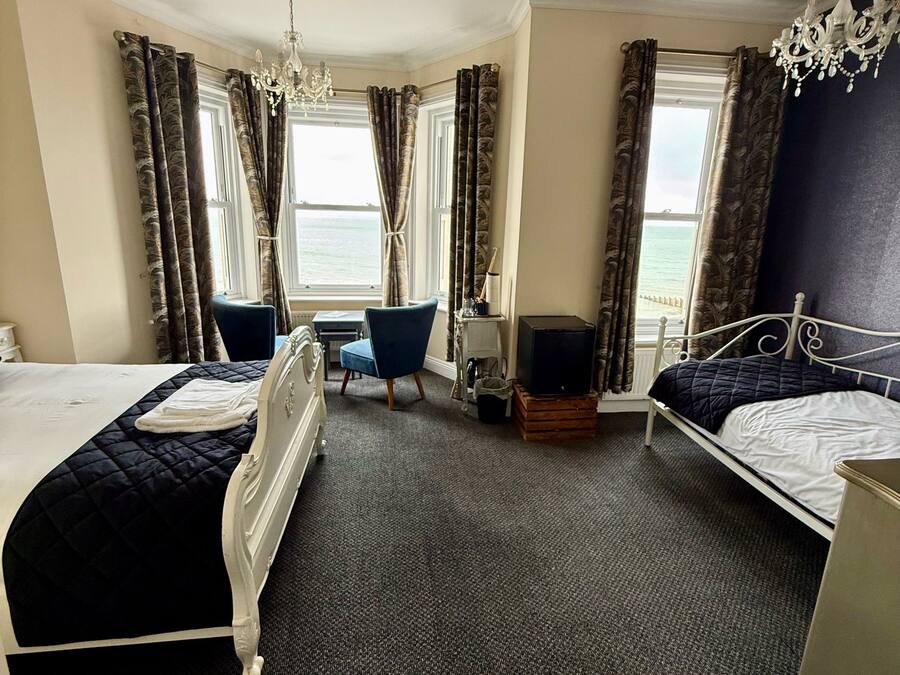 A hotel room with two beds, a large window with curtains, a chandelier, and a view of the sea.