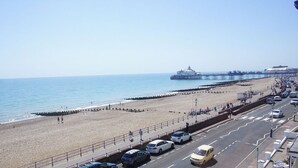 Una playa con un muelle que se adentra en el mar, un paseo marítimo con coches y un edificio con una cúpula.