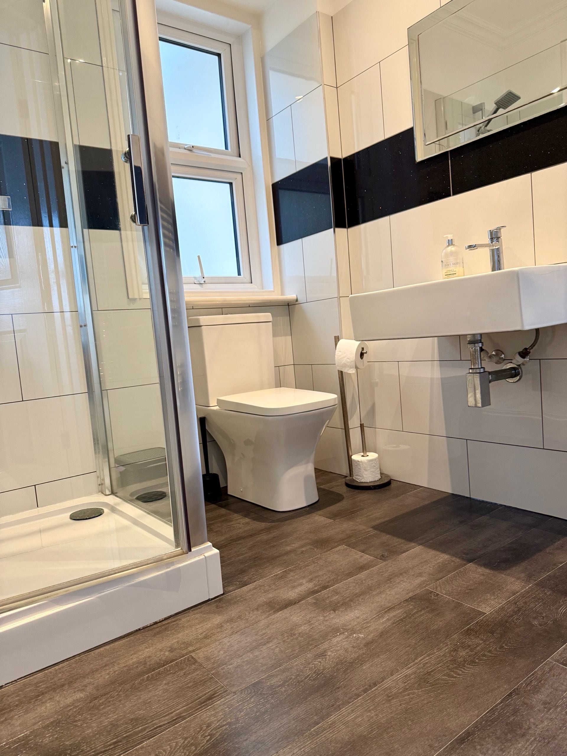 A modern bathroom with a glass-enclosed shower, a toilet, and a sink with a mirror above.