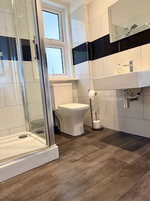 A modern bathroom with a glass-enclosed shower, a toilet, and a sink with a mirror above. - Atlanta Guesthouse (Eastbourne)
