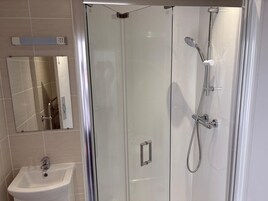 Un baño moderno con ducha de vidrio, un lavamanos blanco y un espejo sobre él.
