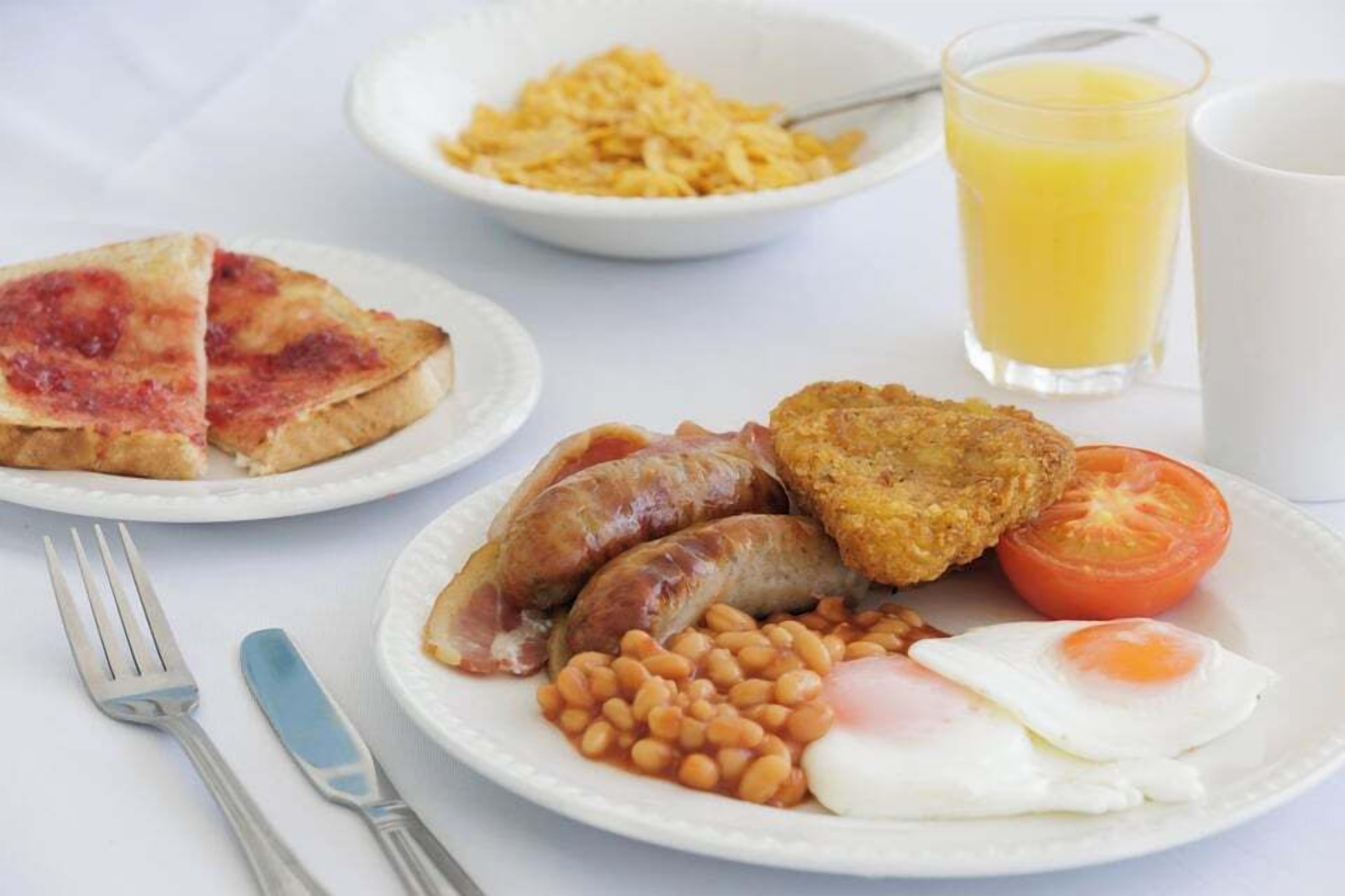 Un plato de desayuno con salchichas, huevos fritos, frijoles y una rebanada de tostada.
