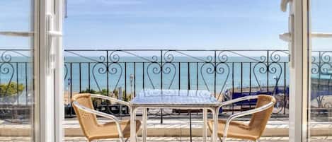 A balcony with a table and two wicker chairs, overlooking a body of water.