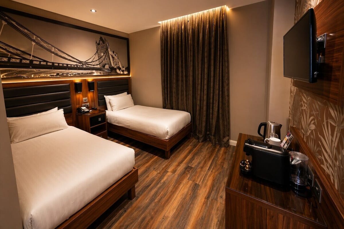 A hotel room with two beds, a flat-screen TV, a coffee maker, and a decorative wall.