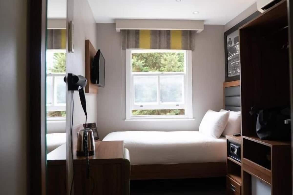 A compact room with a bed, a desk, a wardrobe, and a window with a view of greenery.