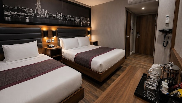 A hotel room with two beds, a nightstand with a phone, a wall-mounted air conditioner, and a tray with toiletries. - London Court Hotel (London)