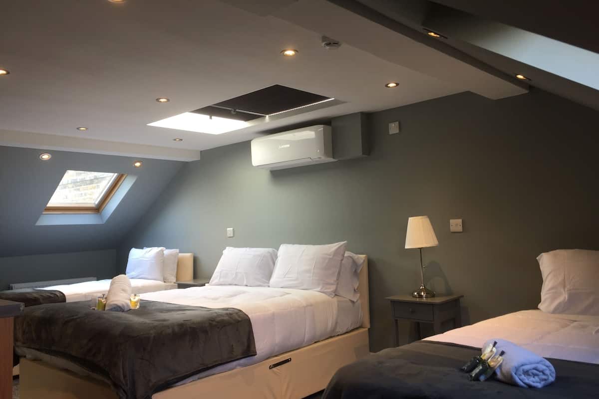 Une chambre d’hôtel avec deux lits, une lucarne, un appareil de climatisation, une lampe de chevet et une petite table avec des articles de toilette.