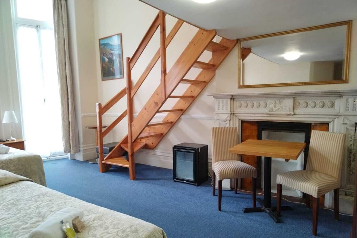 Une chambre d’hôtel avec un escalier en bois, une cheminée, un lit, une petite table, deux chaises et un téléviseur.