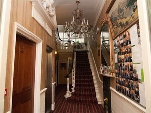 A grand staircase with a red carpet leading to a second floor, flanked by wooden paneling and a chandelier. - St Simeon (London)