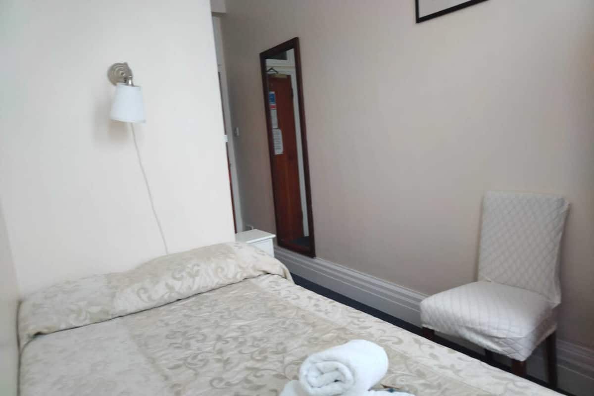 Une chambre d’hôtel avec un lit, une chaise, un miroir et une lampe fixée au mur.