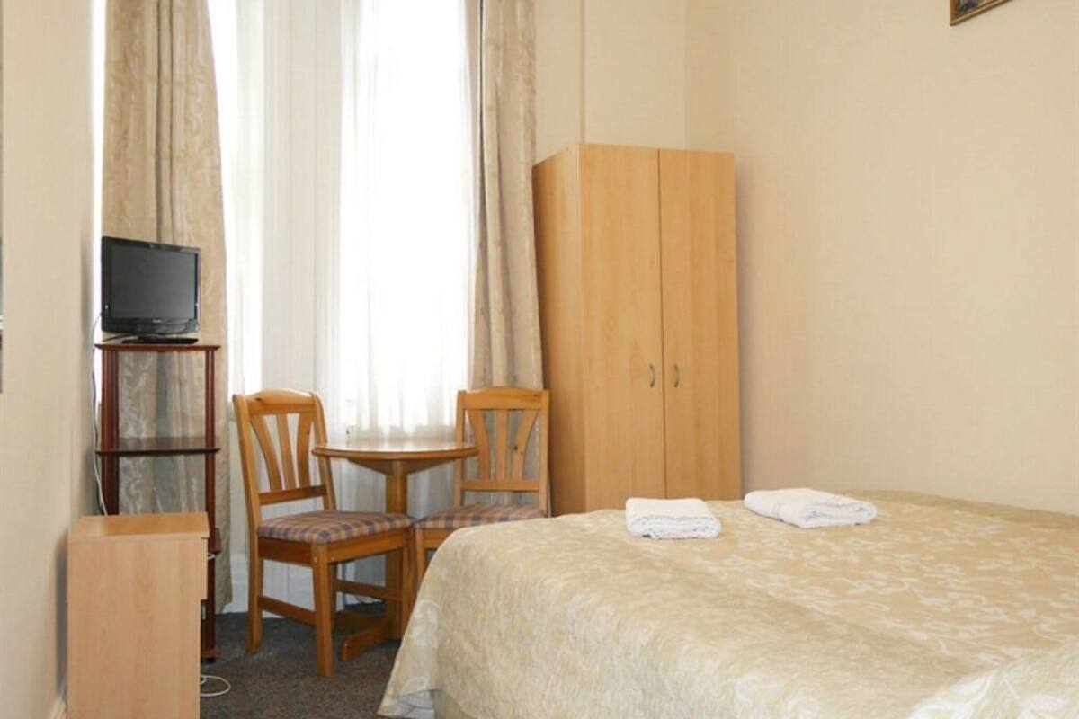Une chambre d’hôtel comprenant un lit, un bureau avec une télévision, une chaise, une armoire et une fenêtre avec des rideaux.