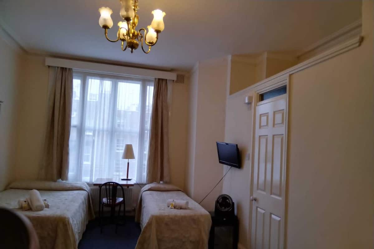 Une chambre d’hôtel avec deux lits, un bureau, une chaise, un téléviseur fixé au mur et une fenêtre avec des rideaux.