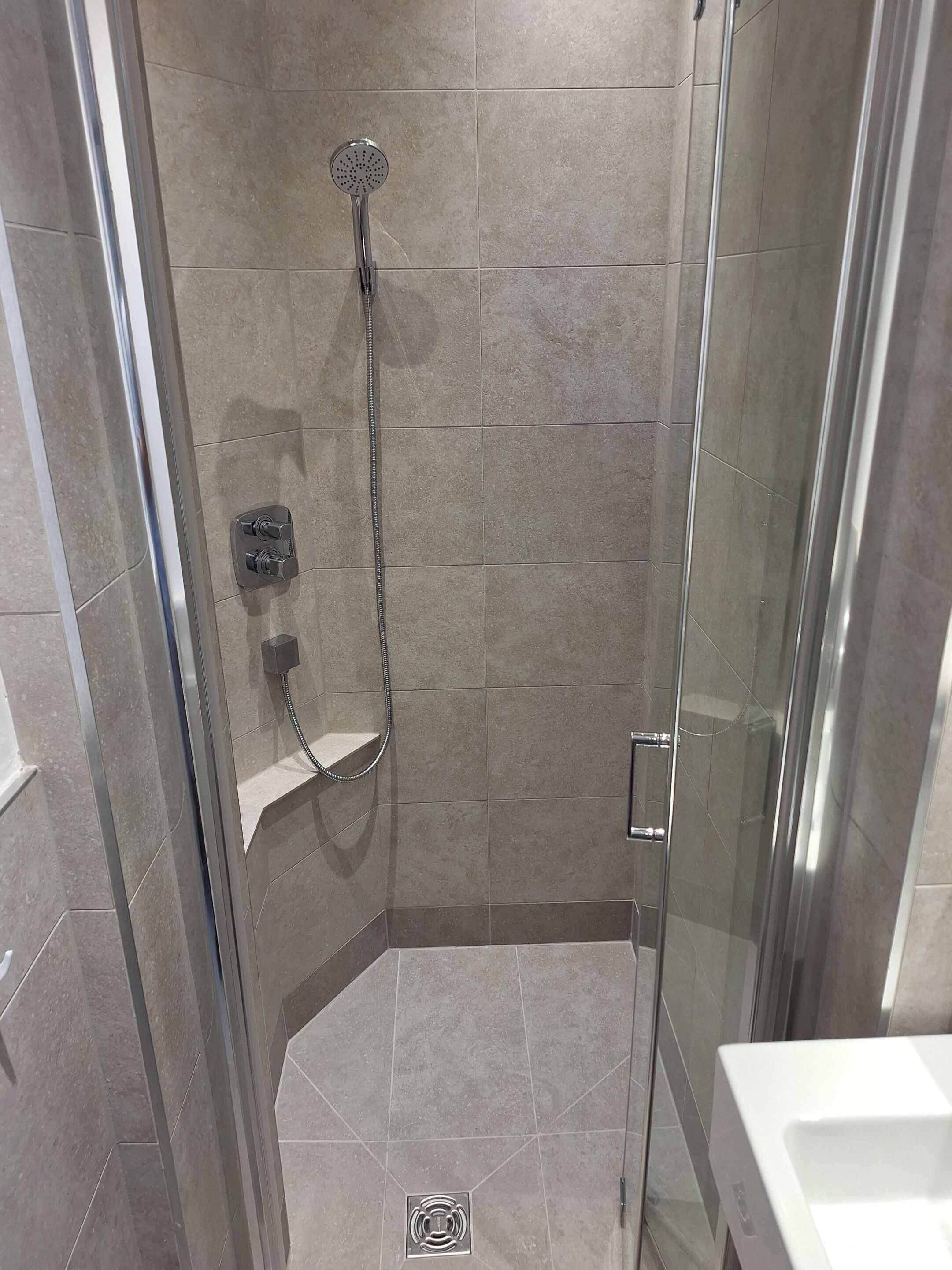 A glass-enclosed shower stall with a handheld showerhead and a wall-mounted control panel.