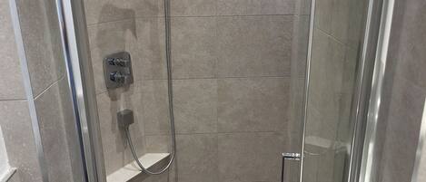 A glass-enclosed shower stall with a handheld showerhead and a wall-mounted control panel.
