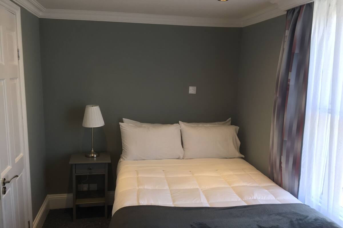 Une chambre à coucher avec un lit, une table de chevet, une lampe et une fenêtre avec des rideaux.