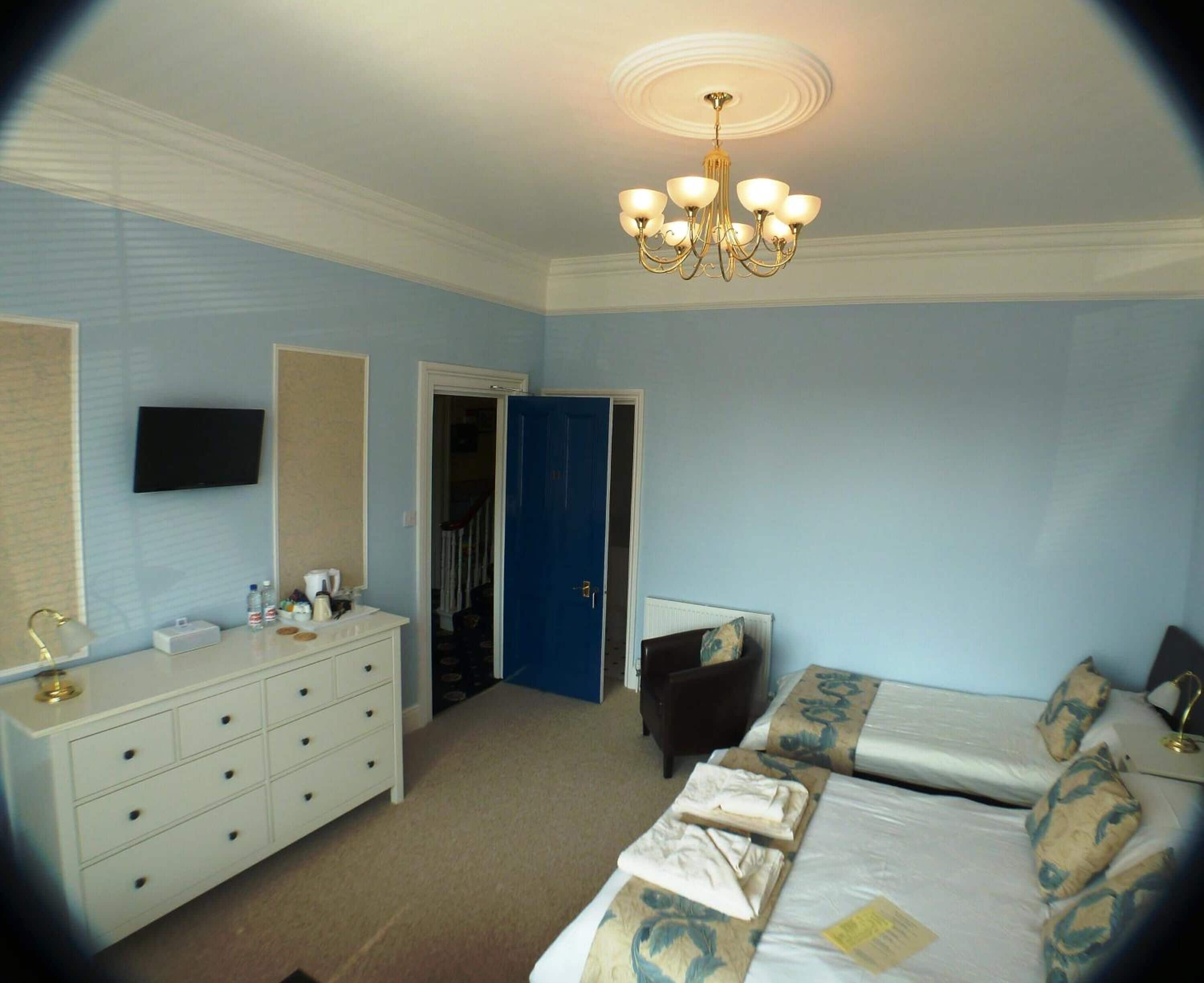 A bedroom with a bed, a dresser, a television, and a chandelier.