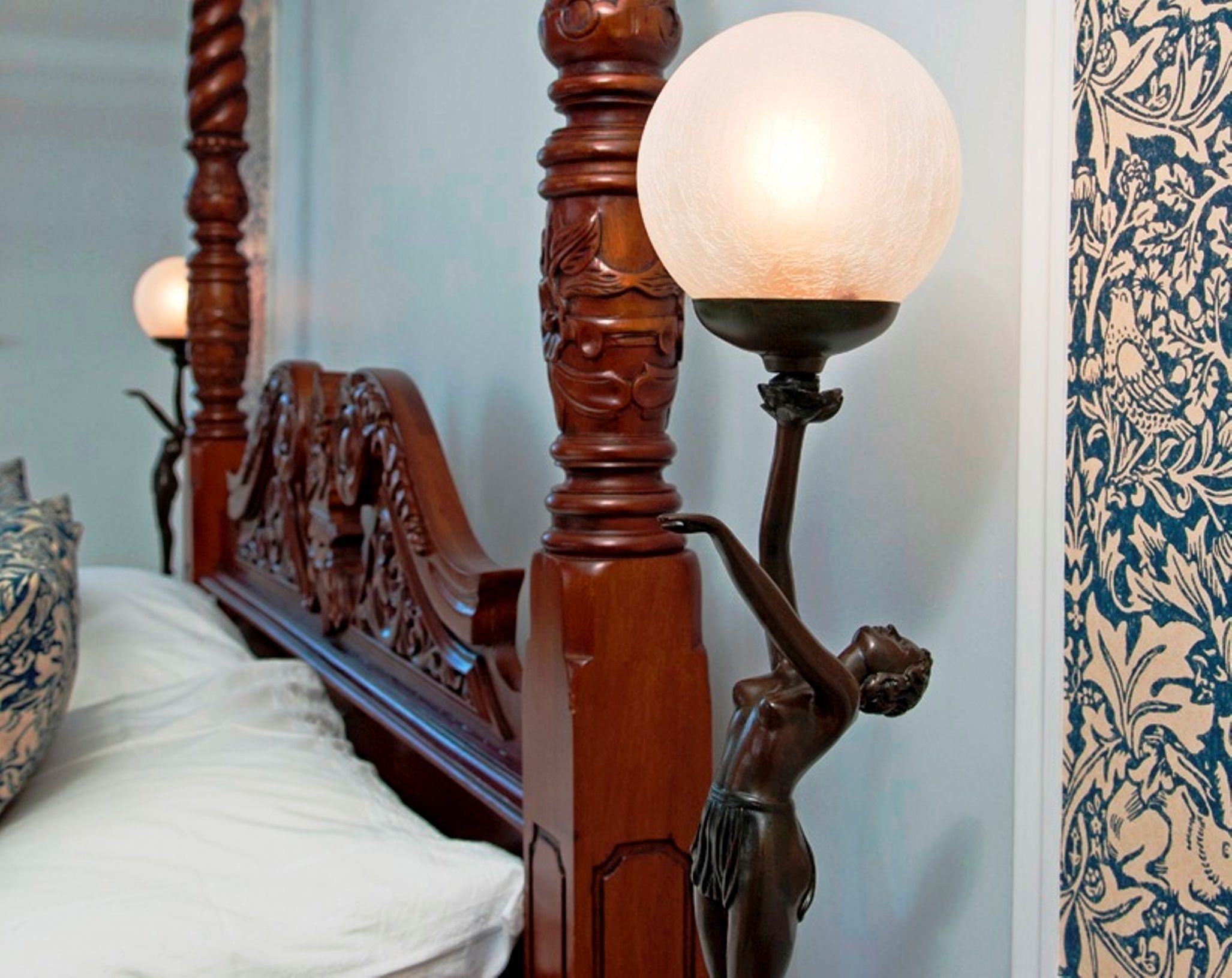 Un lit avec une tête de lit en bois et une table de chevet décorative surmontée d’un lampadaire en forme de globe terrestre.