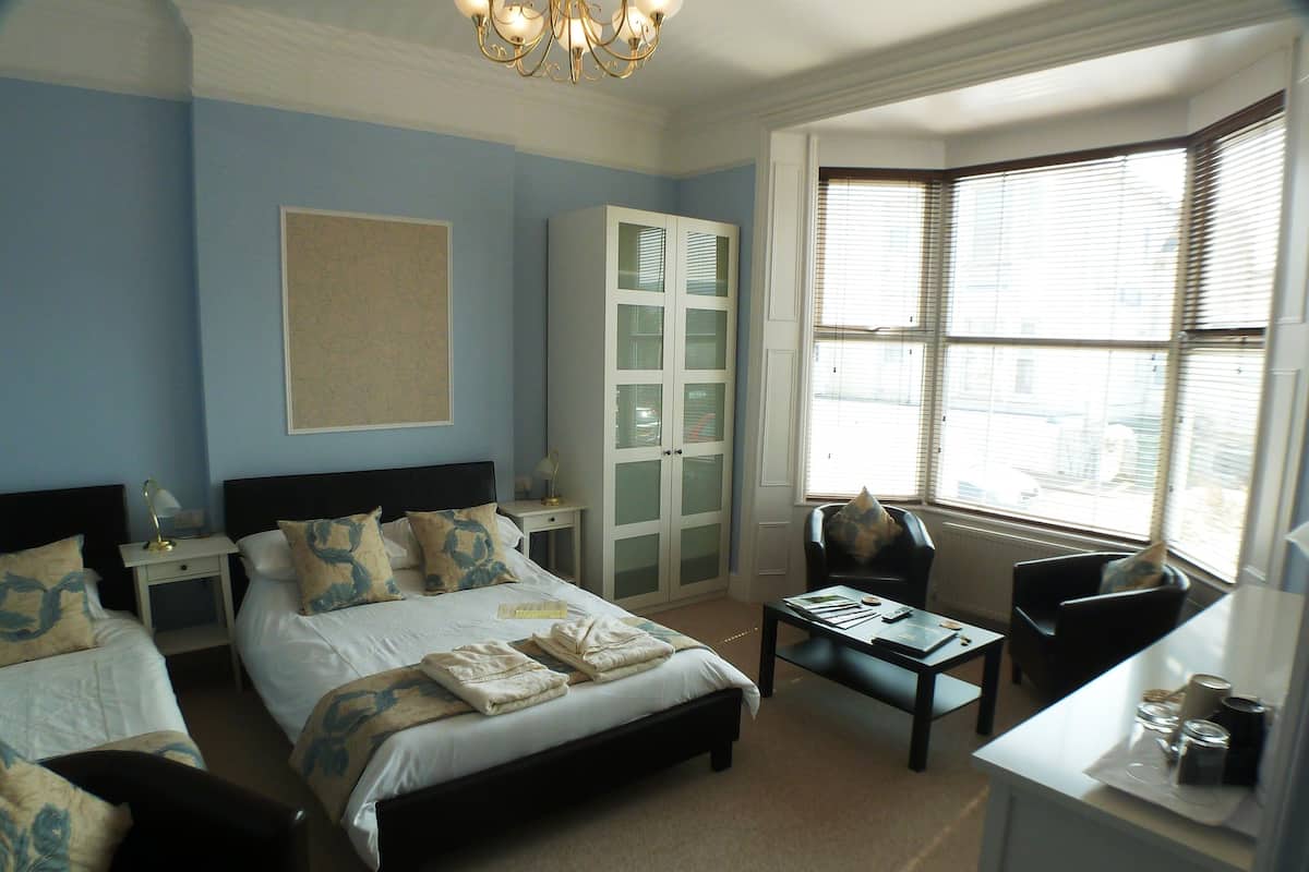 A bedroom with a large bed, two bedside tables, a desk, and a chair. There is a wardrobe with frosted glass doors and a chandelier.