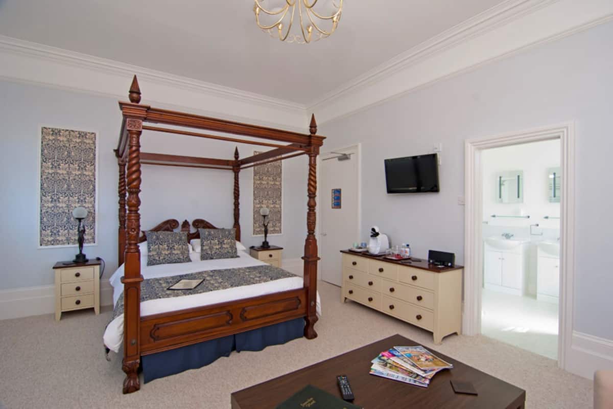 A four-poster bed with a wooden frame, a bedside table with a lamp, a dresser with drawers, and a television on the wall.