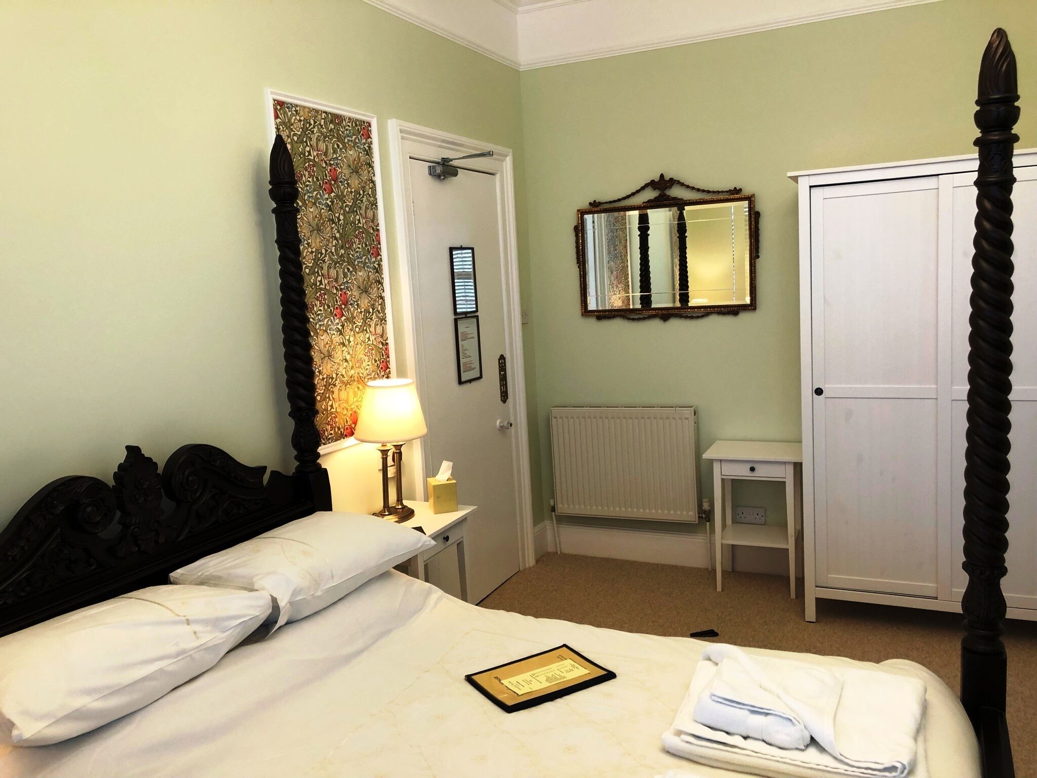 Une chambre d’hôtel avec un lit, une lampe de chevet, un radiateur, une armoire et un miroir au mur.