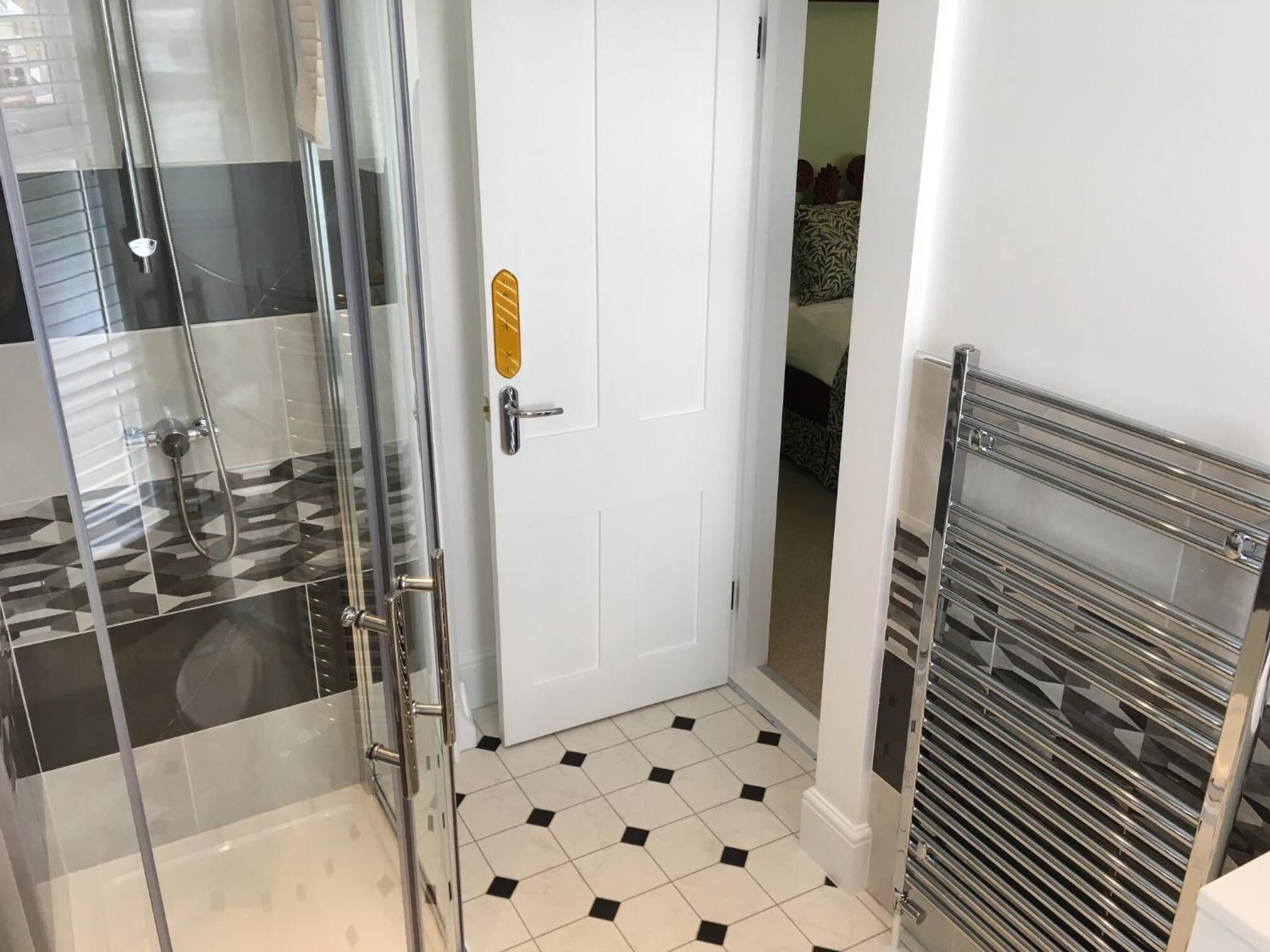 Een badkamer met een douchecabine van glas, een witte deur met een gouden sticker en een betegelde vloer.