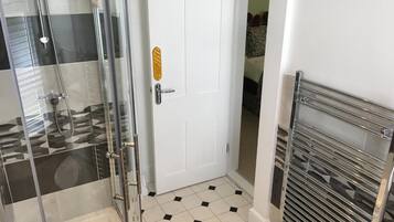 Een badkamer met een douchecabine van glas, een witte deur met een gouden sticker en een betegelde vloer.