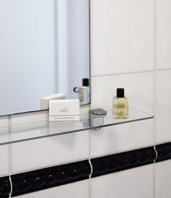 A bathroom with a glass shelf holding a natural cleansing bar and a bottle of Elemis body wash.